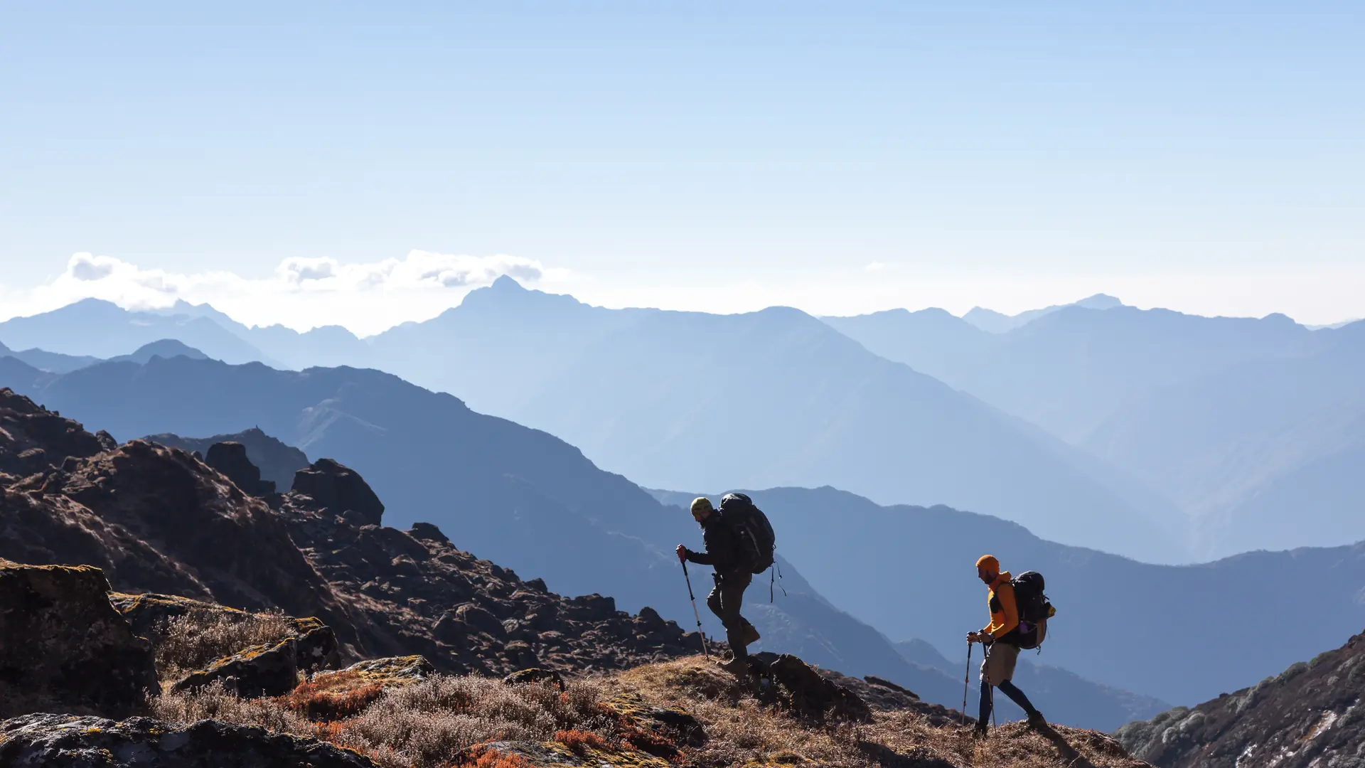 Two hikers with trekking poles on a mountain ridge in front of an alpine panorama